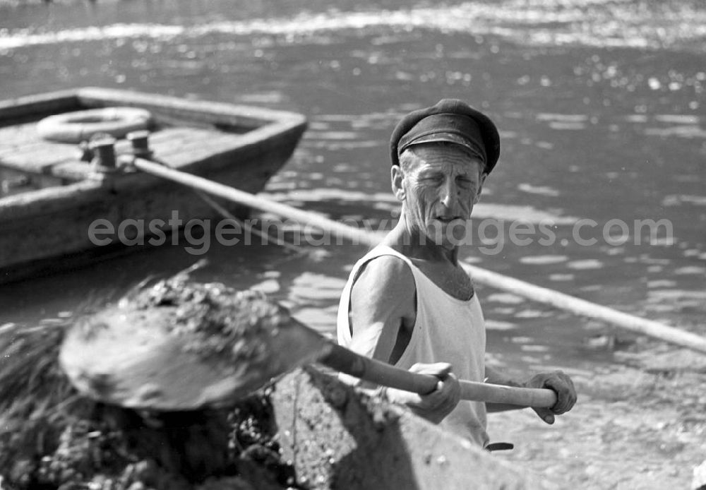 GDR photo archive: Freyburg - Ein Mann mit klassischer Kapitänsmütze schippt an der Unstrut bei Freyburg Sand in einen Container.