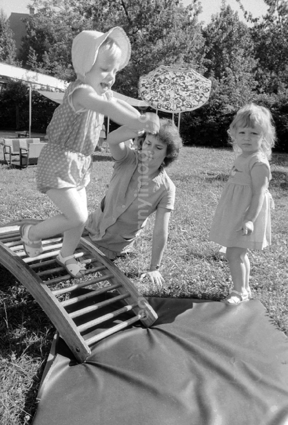 GDR photo archive: Berlin - Children play together with her educator in the garden and do gymnastics about a wooden rung curve in Berlin, the former capital of the GDR, German democratic republic