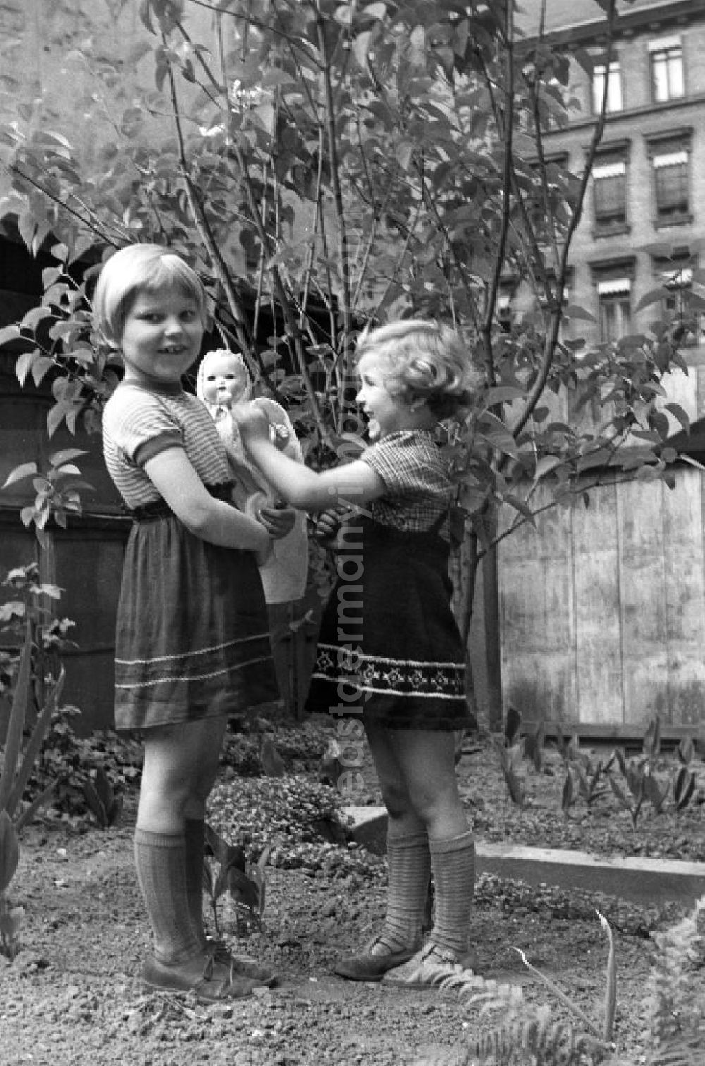 GDR photo archive: Weimar - Zwei Mädchen spielen mit ihrer Puppe auf dem grün bepflanzten Hinterhof eines Altbaus in Weimar. [Bestmögliche Bildqualität nach Vorlage]