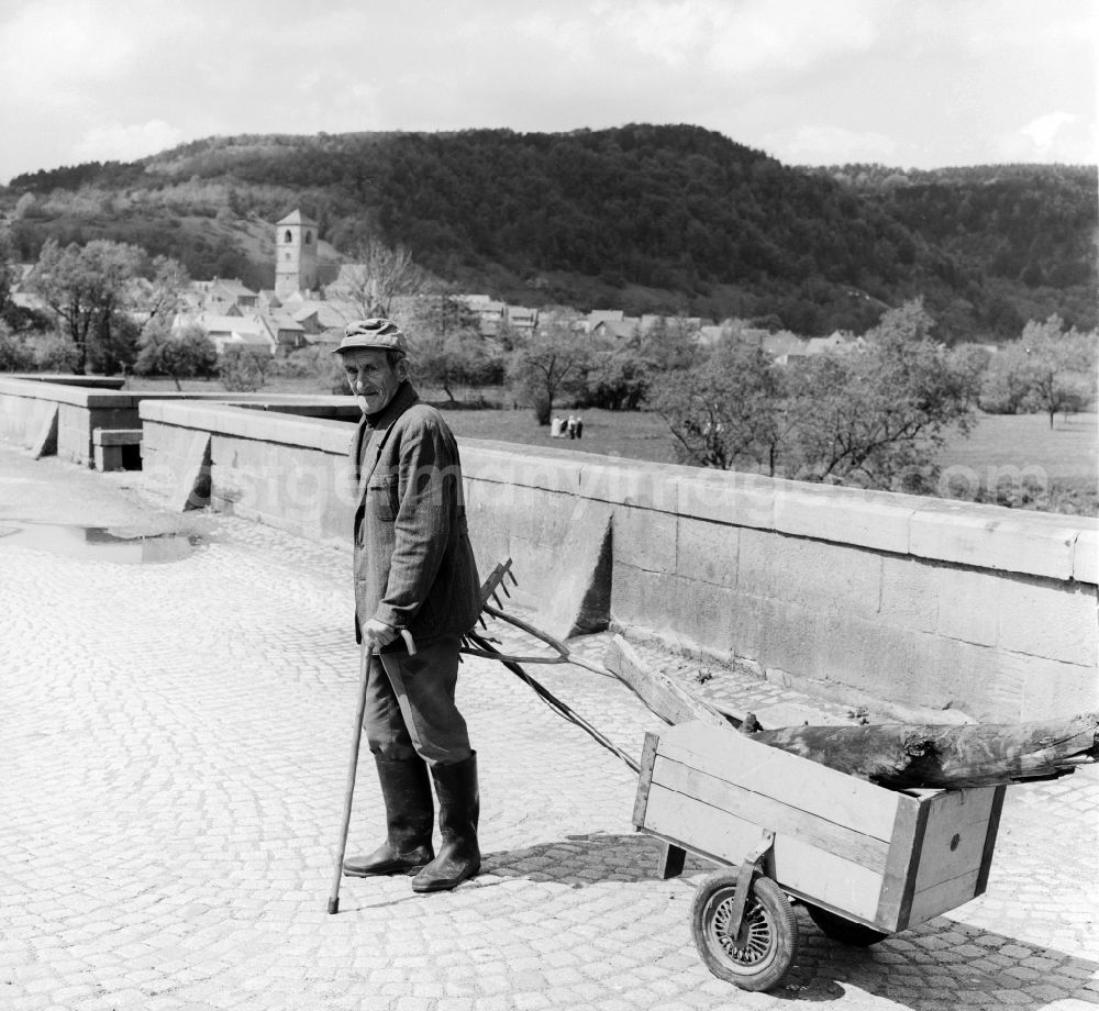 Creuzburg: An old man in overalls with a handcart on the natural stone / stone arch bridge in Creuzburg in Thuringia in the area of the former GDR, German Democratic Republic