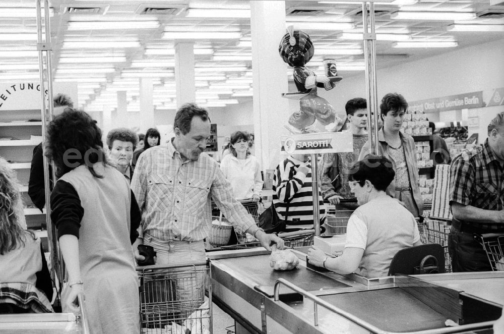 GDR image archive: Berlin - A man at the pay at the cashier in a department store in Berlin, the former capital of the GDR, the German Democratic Republic. The shelves are filled partly with Ostprodukten as well with Western products