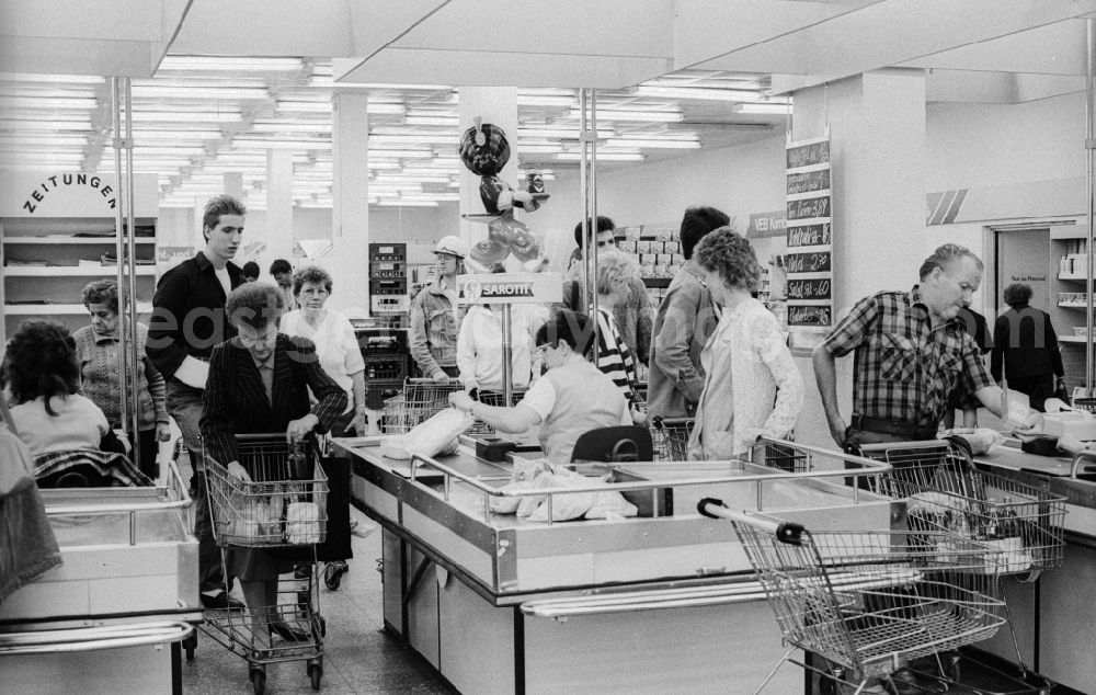 GDR image archive: Berlin - Customer at the pay at the cashier in a department store in Berlin, the former capital of the GDR, the German Democratic Republic. The shelves are filled partly with Ostprodukten as well with Western products