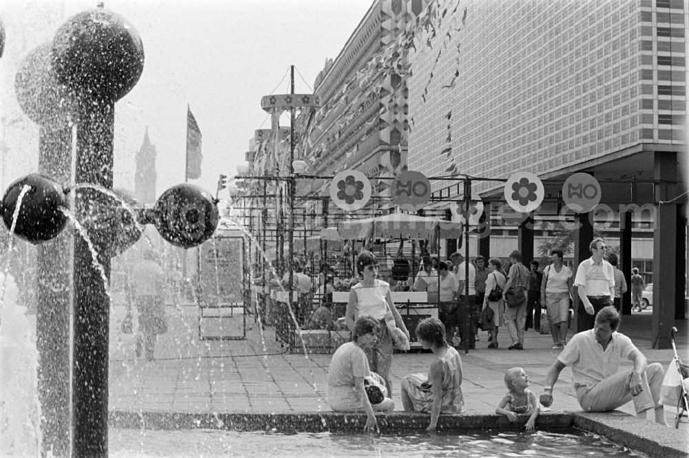 GDR photo archive: Magdeburg - Passers-by at the Kugelbrunnen on Karl-Marx-Strasse ( today Breiter Weg ) in front of the solemnly decorated children's department stores' on the occasion of the 21st Workers' Festival in Magdeburg in the federal state of Saxony-Anhalt in the territory of the former GDR, German Democratic Republic