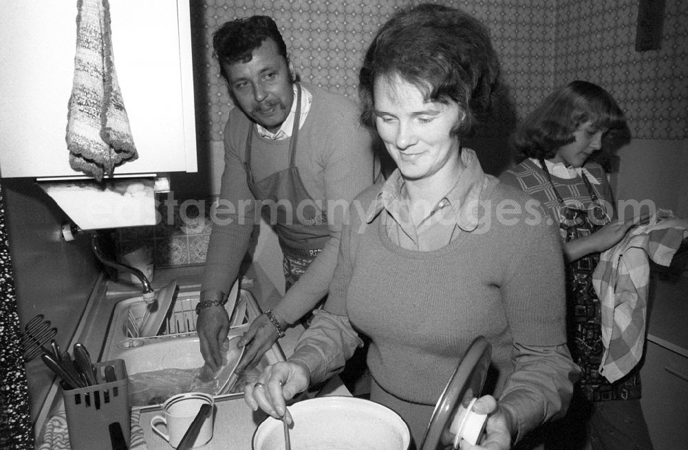 GDR image archive: Berlin - Division of labor in the kitchen with a young family, the mother cooks, the father does the dishes and the daughter dries in Berlin