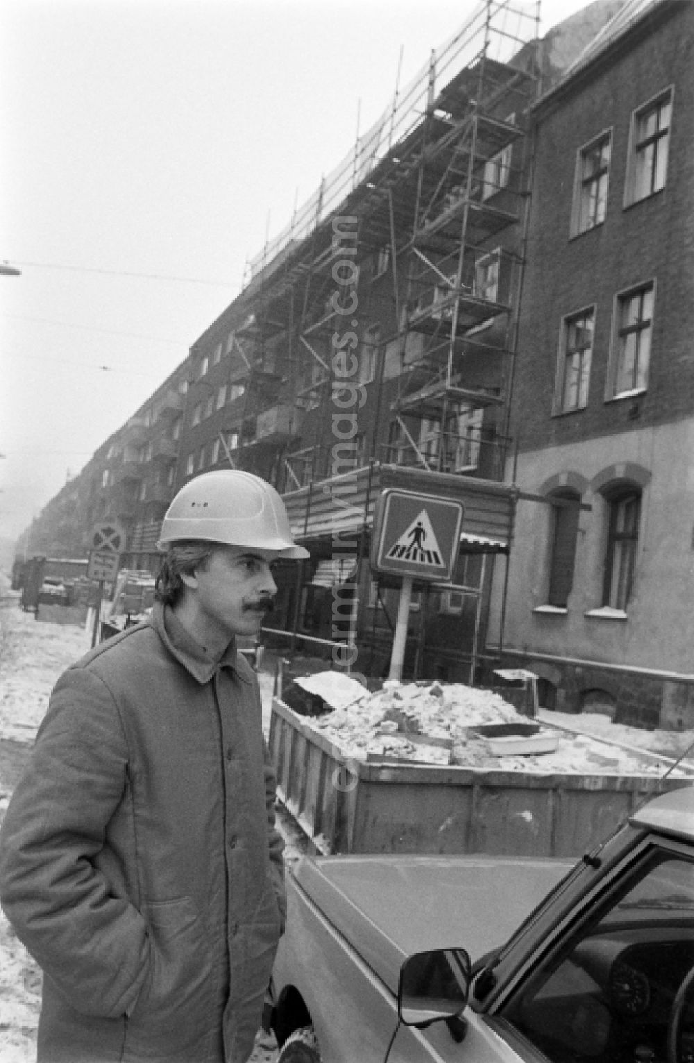 GDR image archive: Berlin - Construction worker with construction helmet stands on street Edisonstrasse in front of apartment building / residential building with scaffolding in the district of Treptow-Koepenick in Berlin, the former capital of the GDR, German Democratic Republic