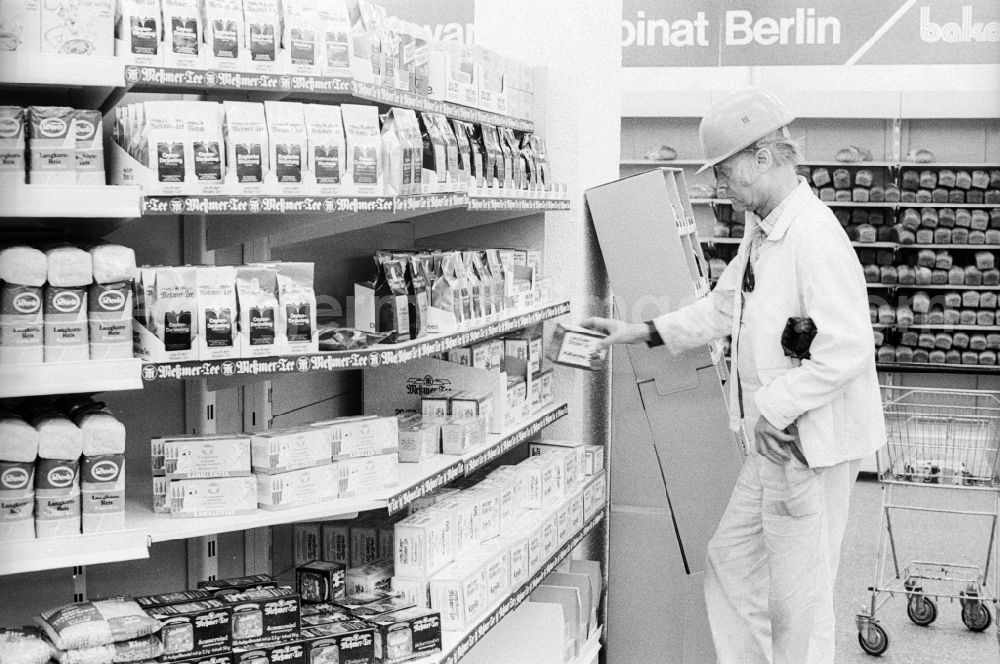 Berlin: A construction worker with helmet standing in front of a shelf in a department store in Berlin, the former capital of the GDR, the German Democratic Republic. The shelves are filled partly with Ostprodukten as well with Western products