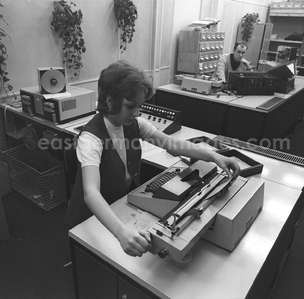 GDR image archive: Berlin - Eine Frau bei der Arbeit vor einer Schreibmaschine im Büro. Sie tippt ein Dokument während ein Kollege zusieht.