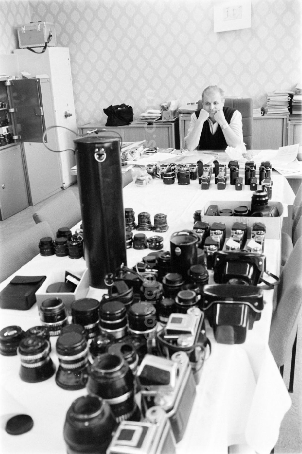 GDR image archive: Berlin - Chief photo reporter Dr. Gerhard Murza in front of photo equipment, lenses and cameras, on a table of the Neues Deutschland ND photo editorial department at Franz-Mehring-Platz in the Friedrichshain district of Berlin