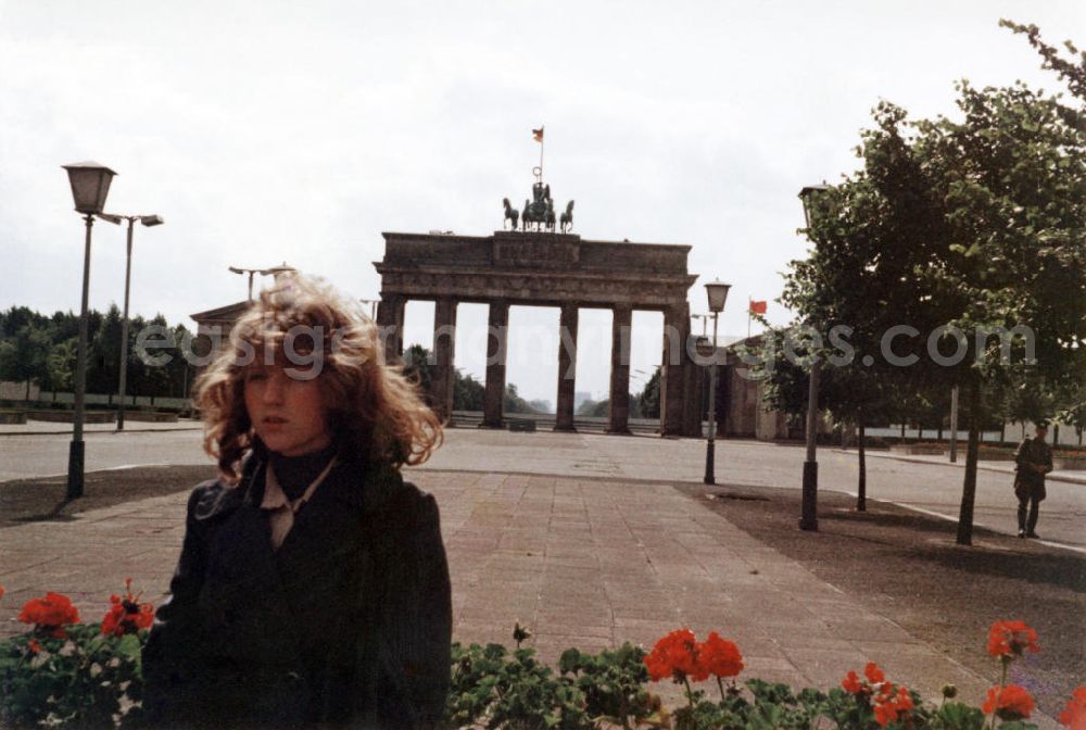 GDR picture archive: Berlin - Eine Frau steht auf dem Pariser Platz vor dem Brandenburger Tor auf der Seite von Ostberlin mit der Mauer im Hintergrund. Ein Soldat / Grenzsoldat (r) schaut der Frau und dem Fotografen zu. Das Brandenburger Tor ist ein Symbol für die Teilung von Deutschland bzw. Berlin.
