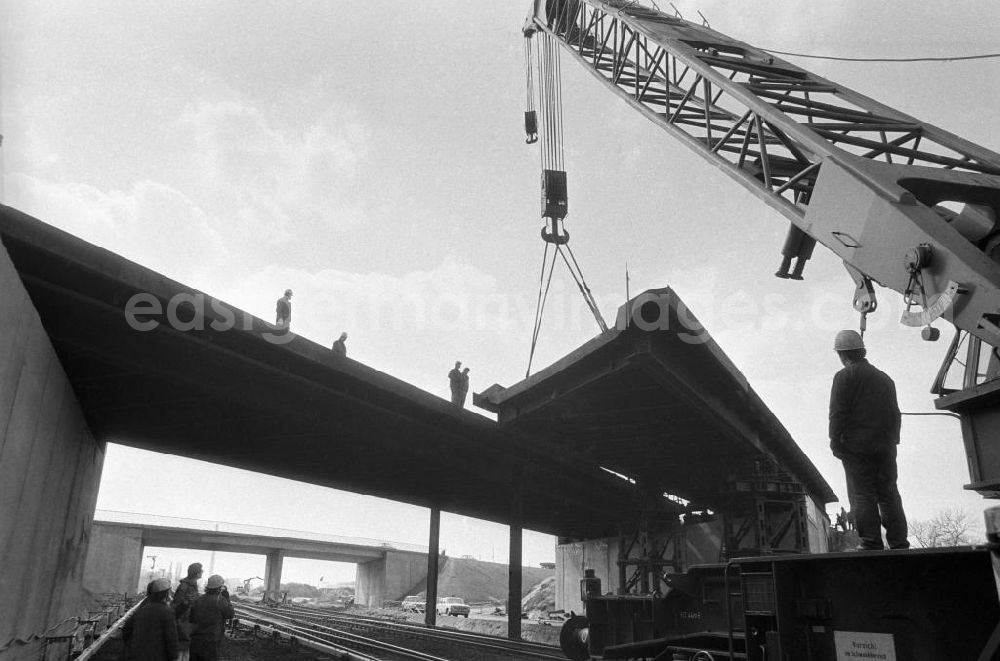 GDR photo archive: Berlin - Brückenarbeiten in Marzahn an der Berliner Chaussee. Brückenstück hängt am Kran, Bauarbeiter schauen zu.