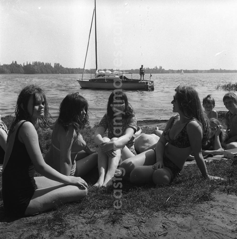 GDR photo archive: Berlin-Schmöckwitz - Campingurlaub am Krossinsee. Urlauber beim Baden und Sonnen. Eine Gruppe junger Frauen posiert für die Kamera. Im Hintergrund wird ein Segelboot zum Auslaufen klar gemacht.