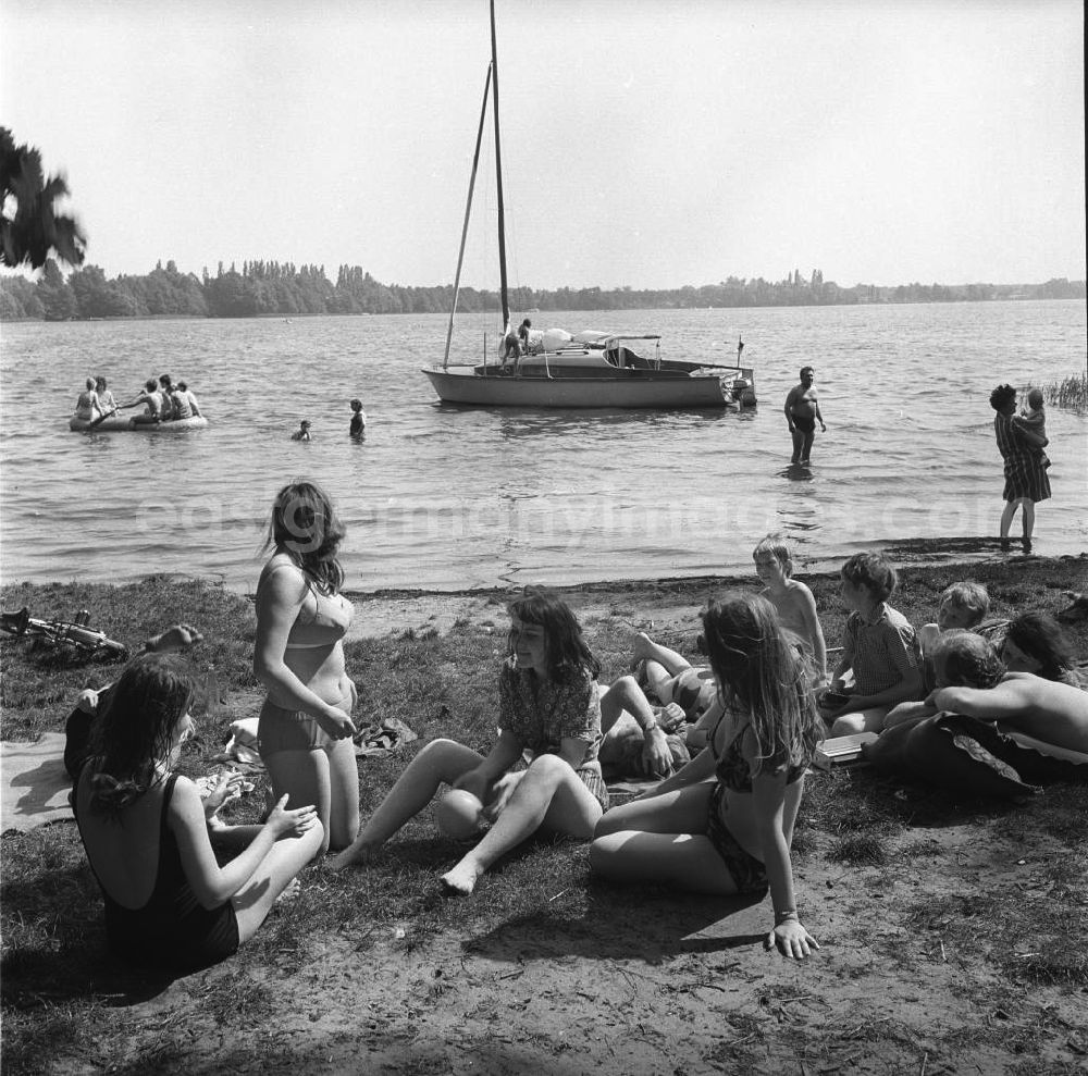 GDR picture archive: Berlin Köpenick - Campingurlaub am Krossinsee. Im Bild: Urlauber beim Baden und Sonnen. Eine Gruppe junger Frauen spielt mit einem Ball. Im Hintergrund wird ein Segelboot zum Auslaufen klar gemacht und das Ufer mit einem Schlauchboot erkundet.
