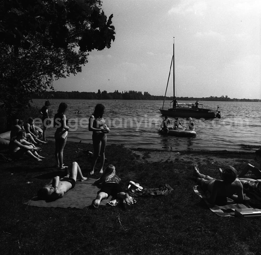 GDR picture archive: Berlin-Köpenick - Campingurlaub am Krossinsee. Im Bild: Urlauber beim Baden und Sonnen. Im Hintergrund ein Schlauchboot und ein auslaufendes Segelschiff.