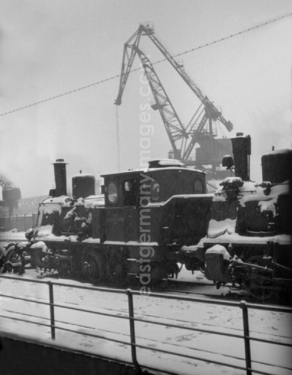 Berlin: Steam locomotive covered with snow in winter as a shunting locomotive in the port area of the Berlin Osthafen in motion on the Alt-Stralau street in the district of Friedrichshain in Berlin East Berlin on the territory of the former GDR, German Democratic Republic