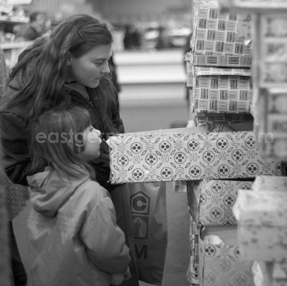 GDR picture archive: Berlin - Ein Mädchen blickt mit ihrer Mutti neugierig in einen Karton mit einer Anziehpuppe in der Spielzeugabteilung im Centrum Warenhaus in Berlin.