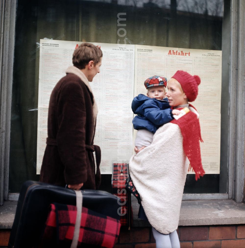 GDR picture archive: Berlin - Eine Familie steht mit ihrem Gepäck vor einem Fahrplan der Deutschen Reichsbahn in Berlin.