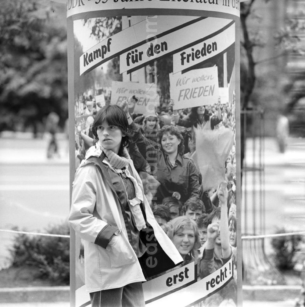 GDR picture archive: Berlin - Zum Pfingsttreffen der FDJ in Berlin steht ein Mädchen an einer Litfaßsäule mit sozialistischer Propaganda. Kampf für den Frieden heißt es auf den Plakaten.