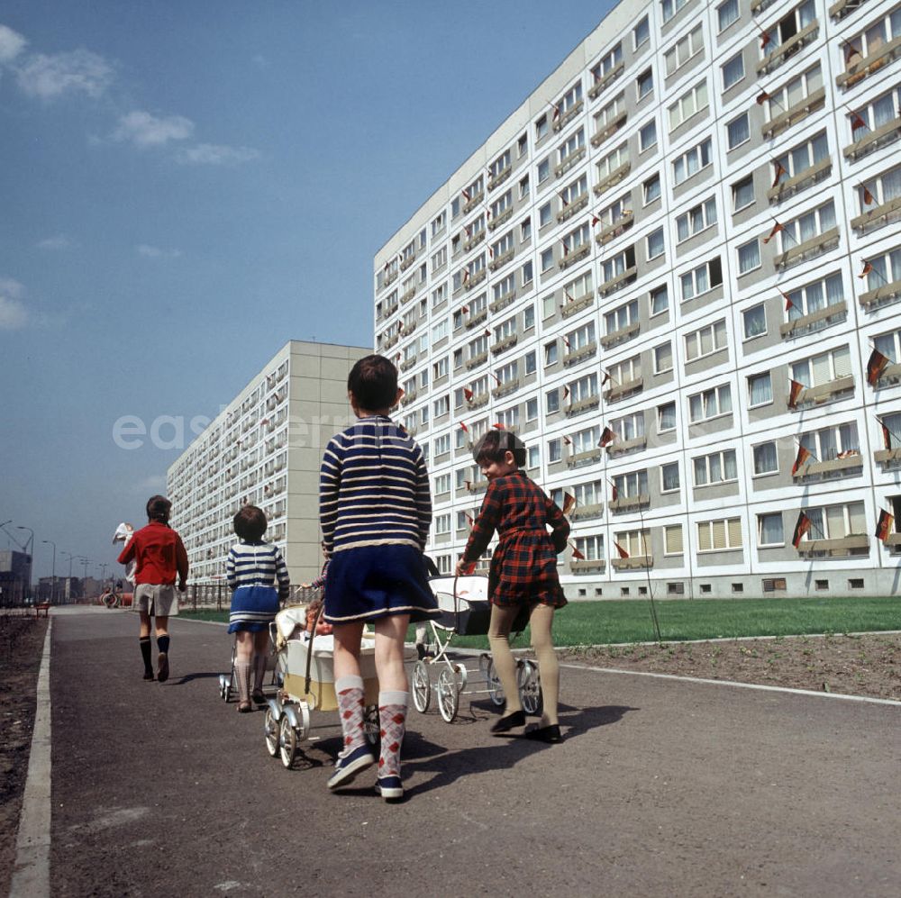 GDR image archive: Berlin - Kinder gehen mit ihren Puppenwagen spazieren, aufgenommen im Neubauviertel an der Spandauer Straße / Ecke Karl-Liebknecht-Straße. Die Häuser sind zum Maifeiertag mit Fahnen festlich geschmückt. Der bestehende Wohnungsmangel entwickelte sich in der DDR seit den 6