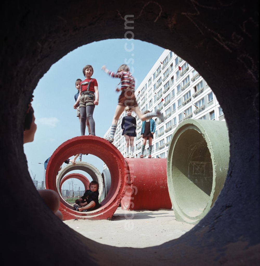 GDR photo archive: Berlin - Kinder spielen auf bunt angemalten Betonröhren, aufgenommen im Neubauviertel an der Spandauer Straße / Ecke Karl-Liebknecht-Straße. Die Häuser sind zum Maifeiertag mit Fahnen festlich geschmückt. Der bestehende Wohnungsmangel entwickelte sich in der DDR seit den 6