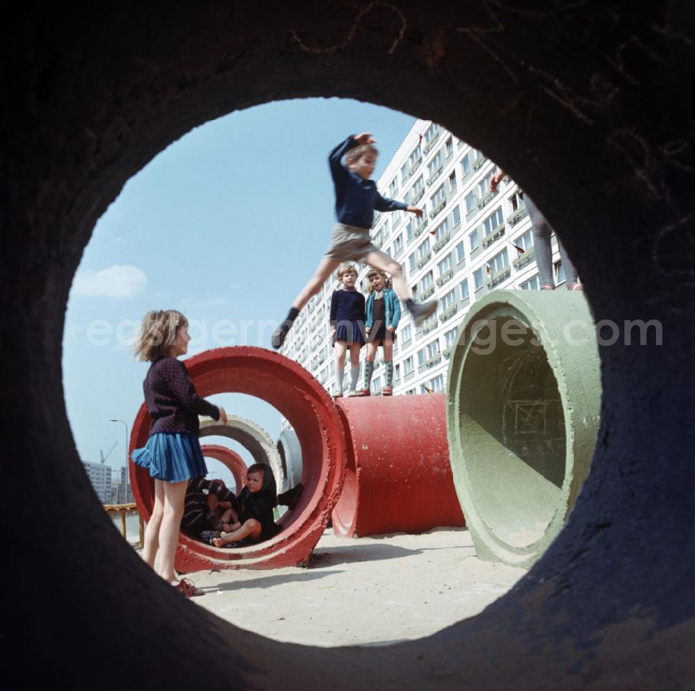 Berlin: Kinder spielen auf bunt angemalten Betonröhren, aufgenommen im Neubauviertel an der Spandauer Straße / Ecke Karl-Liebknecht-Straße. Die Häuser sind zum Maifeiertag mit Fahnen festlich geschmückt. Der bestehende Wohnungsmangel entwickelte sich in der DDR seit den 6