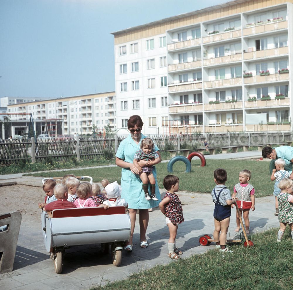 GDR image archive: Halle an der Saale - Eine Erzieherin trägt ein kleines Kind zu einem Kinderwagen in einem Kindergarten in Halle-Neustadt. Am Standort der Chemieindustrie der DDR wurde in den 1960er und 197