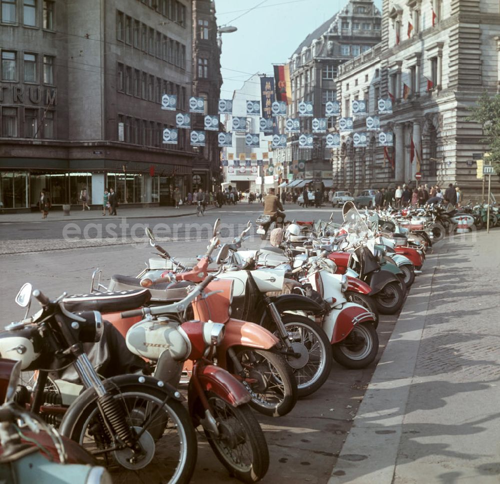 GDR picture archive: Leipzig - Motorräder / Mopeds u.a. vom Typ Spatz, Schwalbe, MZ, Simson usw. stehen nebeneinander am Straßenrand. In der Fußgängerzone wird für die Ausstellungen der Herbstmesse geworben.