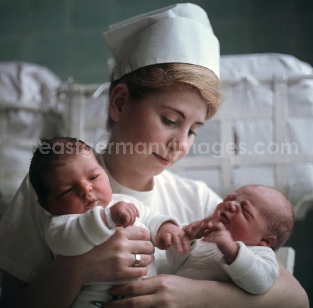 GDR photo archive: Berlin - Eine Krankenschwester in einem Krankenhaus in Berlin-Kaulsdorf hält zwei Neugeborene in ihren Armen.