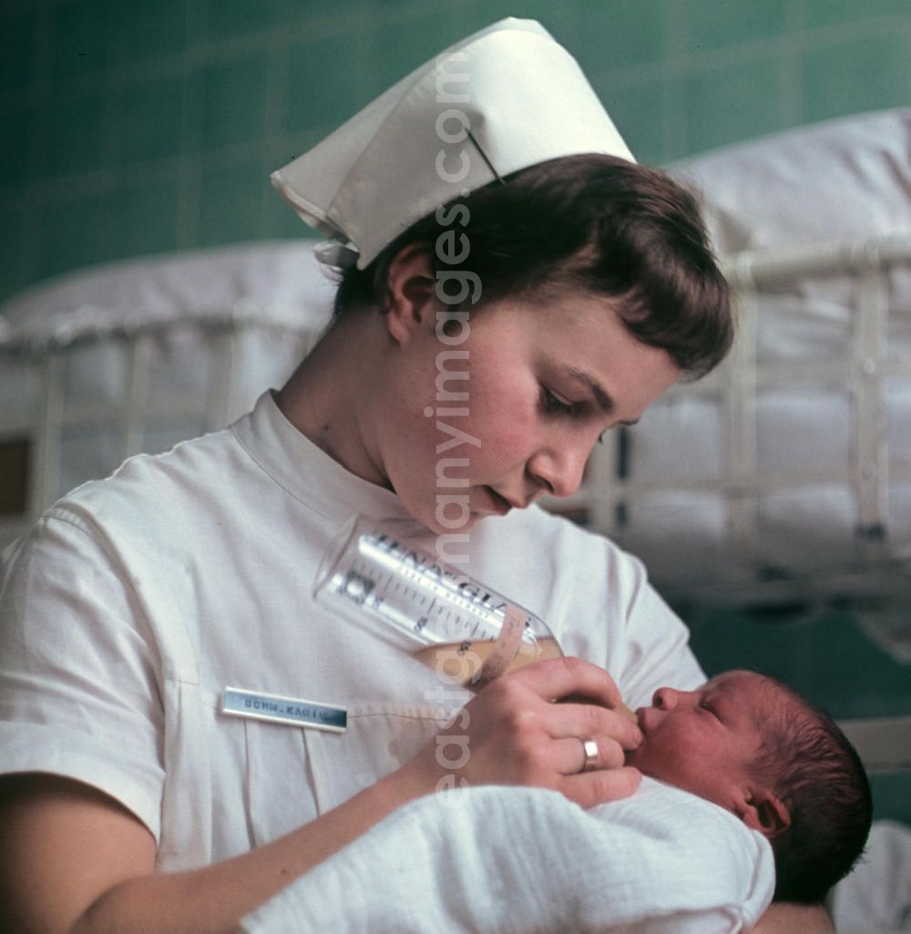GDR photo archive: Berlin - Eine Krankenschwester in einem Krankenhaus in Berlin-Kaulsdorf gibt einem Neugeborenen das Fläschchen.