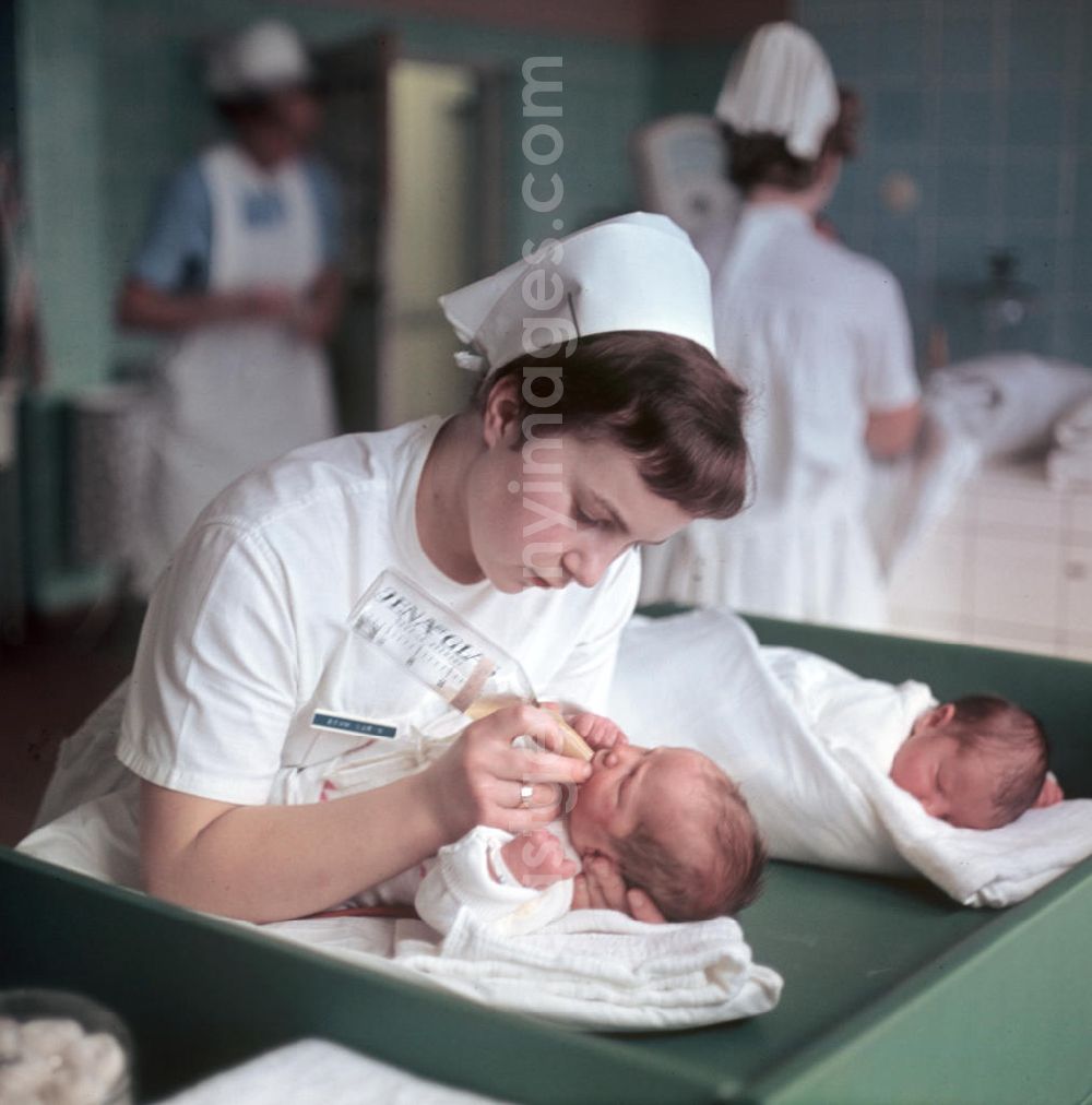 GDR picture archive: Berlin - Eine Krankenschwester in einem Krankenhaus in Berlin-Kaulsdorf gibt einem Neugeborenen das Fläschchen.