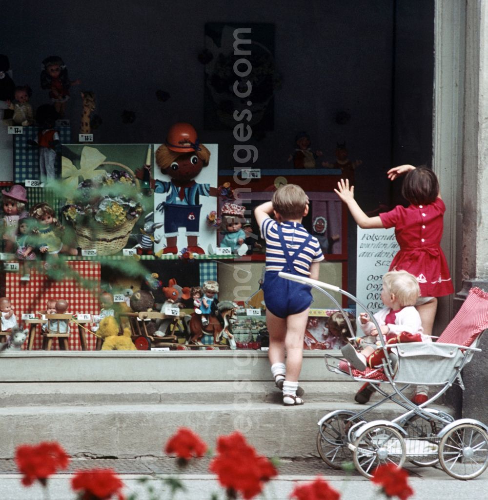 GDR picture archive: Berlin - Kinder schauen neugierig durch das Schaufenster eines Spielzeugladens in Berlin, in dem vor allem Puppen, Teddys und ein Puppentheater ausgestellt sind.
