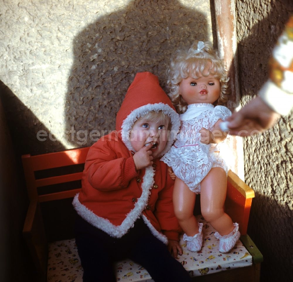 GDR picture archive: Berlin - Kleines Kind in Weihnachtsmann-Jacke mit Puppe, aufgenommen in den 197