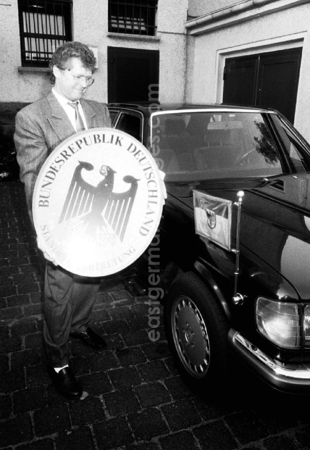 GDR photo archive: Berlin - Demontage vom Vertretungsschild der BRD (Ständige Vertretung) in der Hannoverschen Strasse. Mann hält das Schild und steht dabei neben einem Mercedes-Benz mit Wimpel-Fahne.