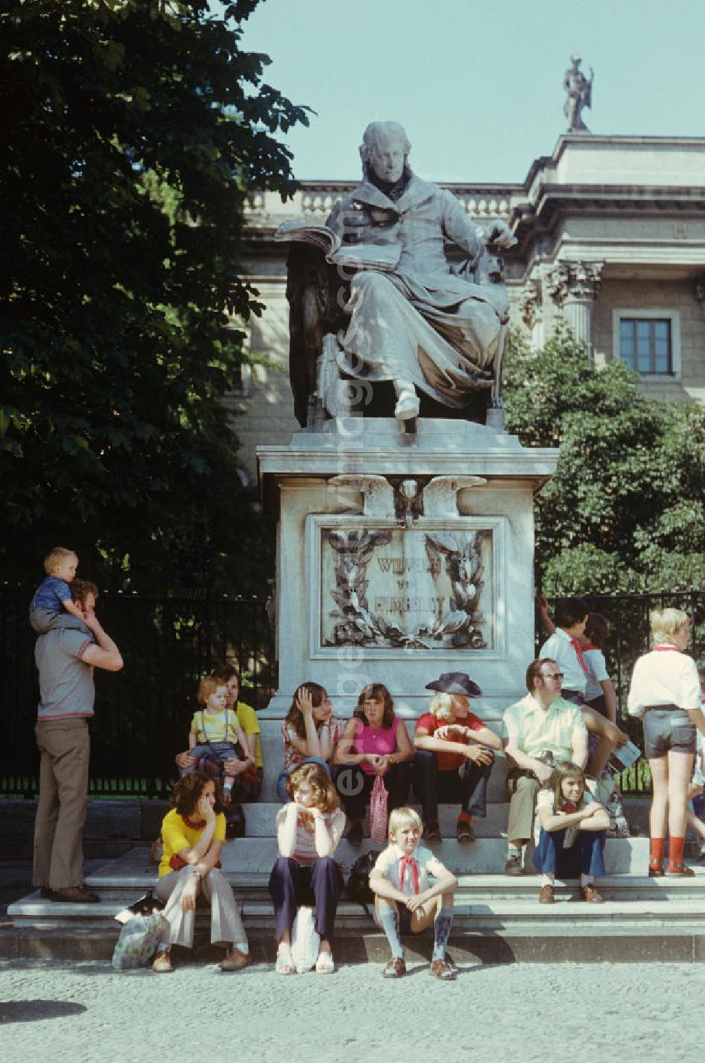 GDR picture archive: Berlin - Junge Pioniere und Touristen sitzen auf den Stufen des Denkmals für Wilhelm von Humboldt, das vor dem Hauptgebäude der Humboldt-Universität Unter den Linden in Berlin steht.