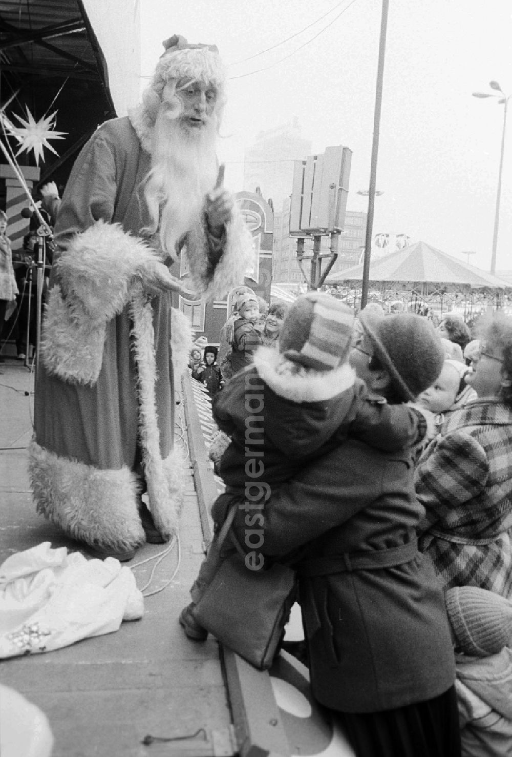 GDR picture archive: Berlin - A mother lifts her child on the stage to the Santa Claus on the Berlin Christmas fair in Berlin, the former capital of the GDR, German democratic republic. Today there stands at this point the shopping centre Alexa