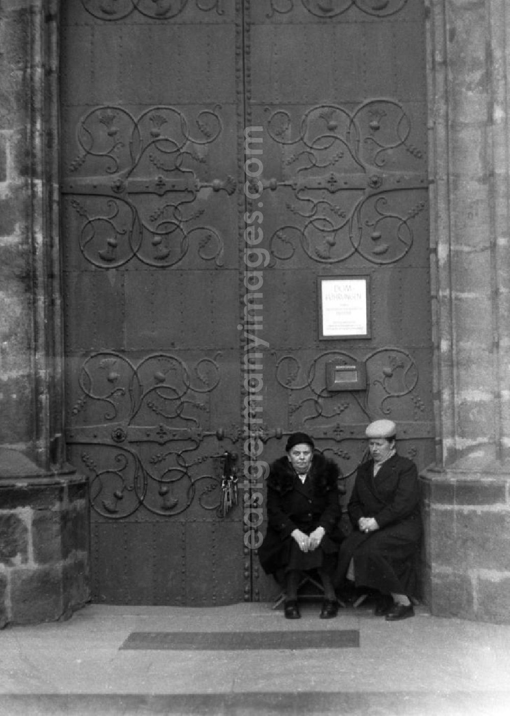 GDR picture archive: Meißen - Zwei ältere Damen sitzen vor dem Portal des Meißner Doms. Auf einem Aushang werden Domführungen angeboten, im Schloß hängt ein riesiger Schlüsselbund.