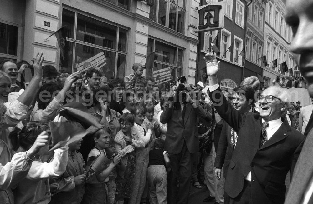 GDR photo archive: Greifswald - Besuch von Erich Honecker anlässlich der Domweihe. Passanten / Schaulustige auf Marktplatz, stehen hinter Absperrung und geben Applaus. Honecker steht davor lacht und winkt, dahinter Klaus Ewald, Oberbürgermeister Greifswald. DDR-Flaggen hängen an Gebäuden.