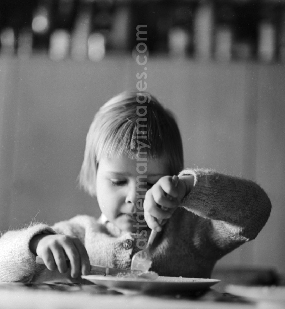 GDR picture archive: Berlin - A child eats with fork and knife in Berlin, the former capital of the GDR, the German Democratic Republic