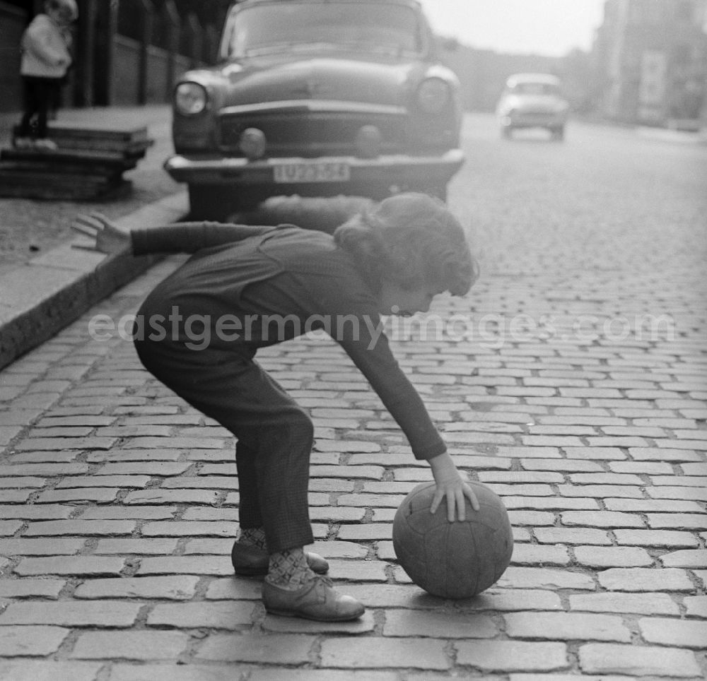 GDR image archive: Berlin - A child plays with a ball on the street in Berlin. In the background is a parked Auo type Volga
