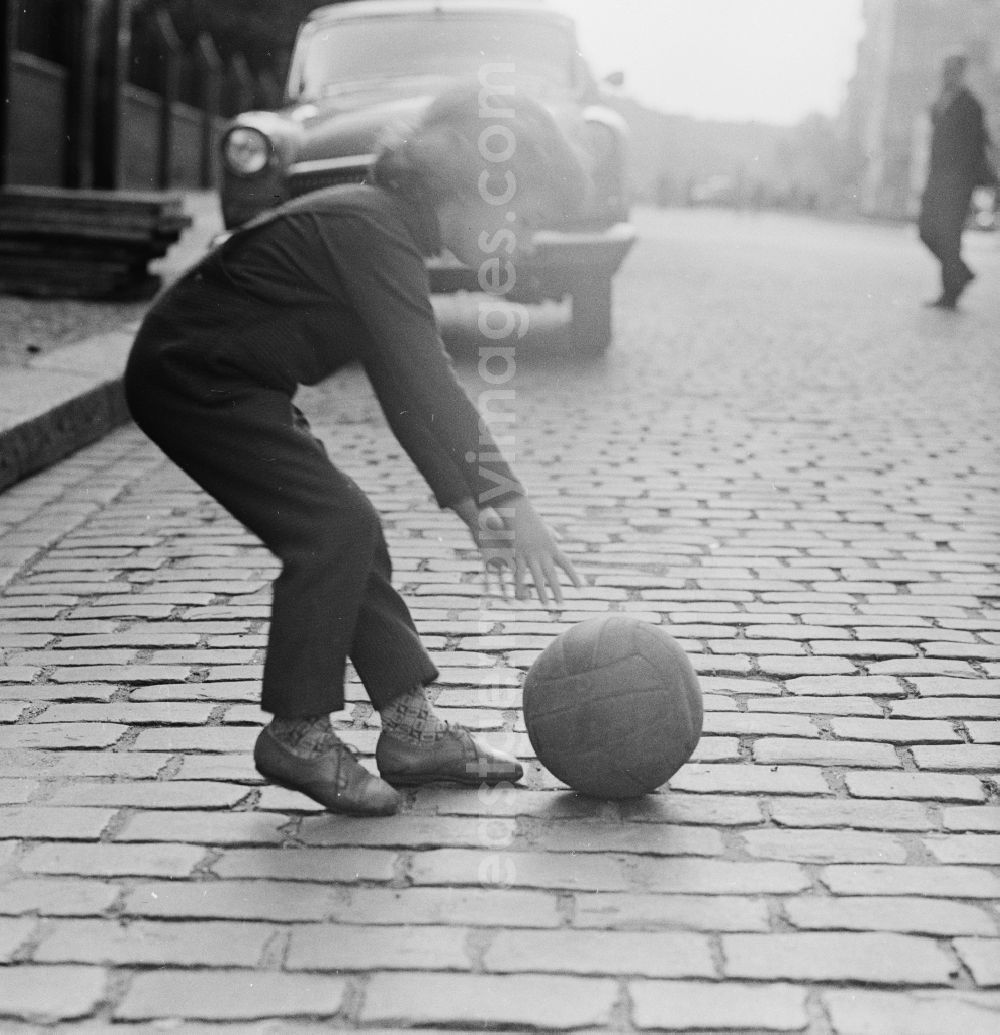 GDR photo archive: Berlin - A child plays with a ball on the street in Berlin. In the background is a parked Auo type Volga