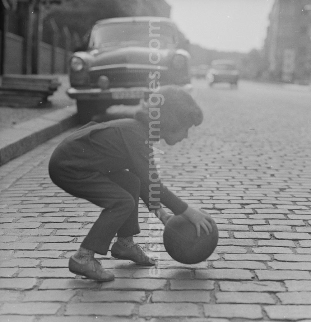 GDR picture archive: Berlin - A child plays with a ball on the street in Berlin. In the background is a parked Auo type Volga