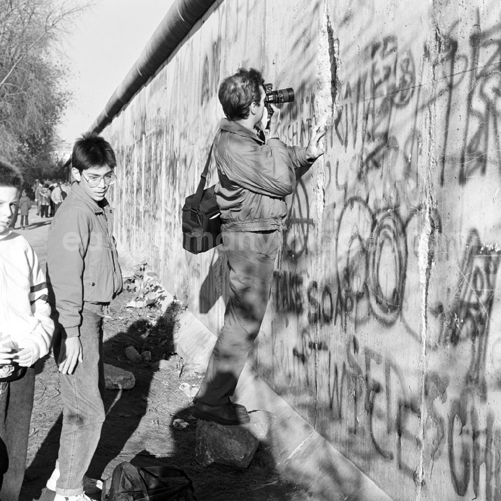 GDR photo archive: Berlin - Mitte - A man photographs through a crack in the Berlin Wall in Berlin
