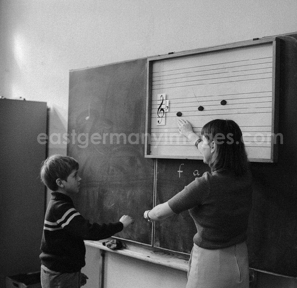GDR photo archive: Berlin - A student stands at the blackboard and the music teacher explains the scale in Berlin. On the blackboard are staves with clef and notes