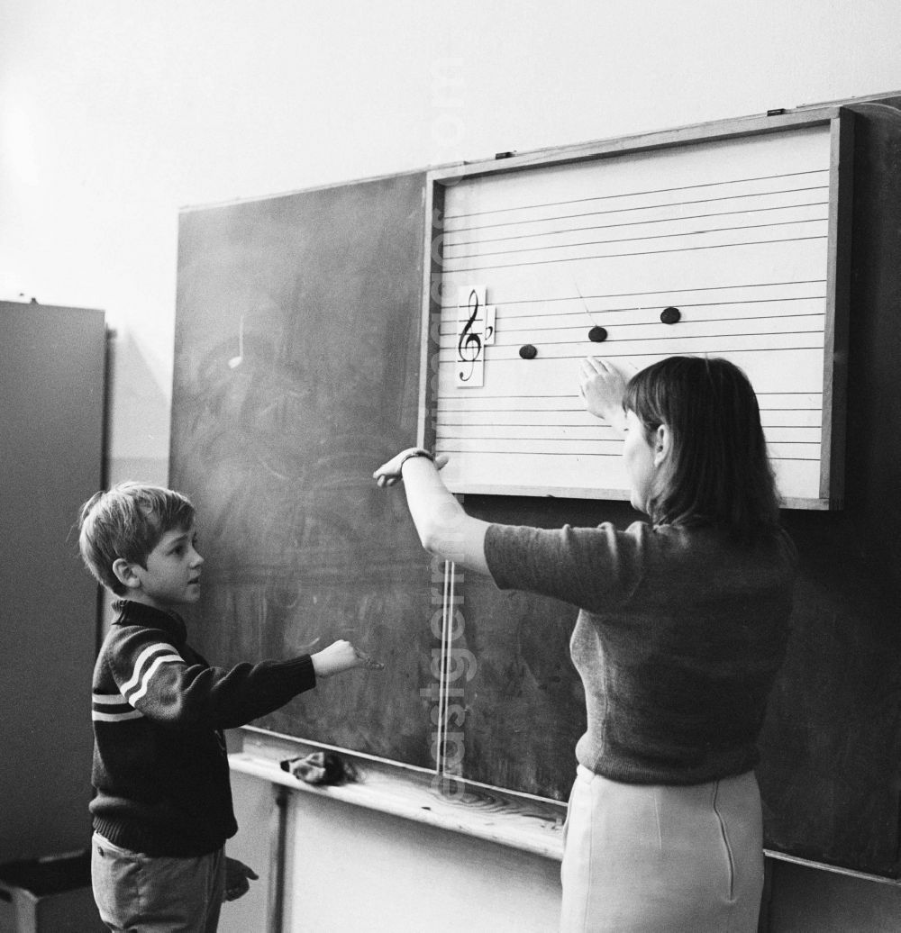 Berlin: A student stands at the blackboard and the music teacher explains the scale in Berlin. On the blackboard are staves with clef and notes