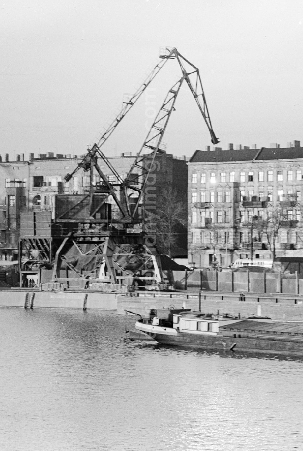 Berlin: A heavy-duty crane at the riverside in the east port - Port Industry in Berlin. In the background houses at Stralauer Allee. In the foreground a transport barge