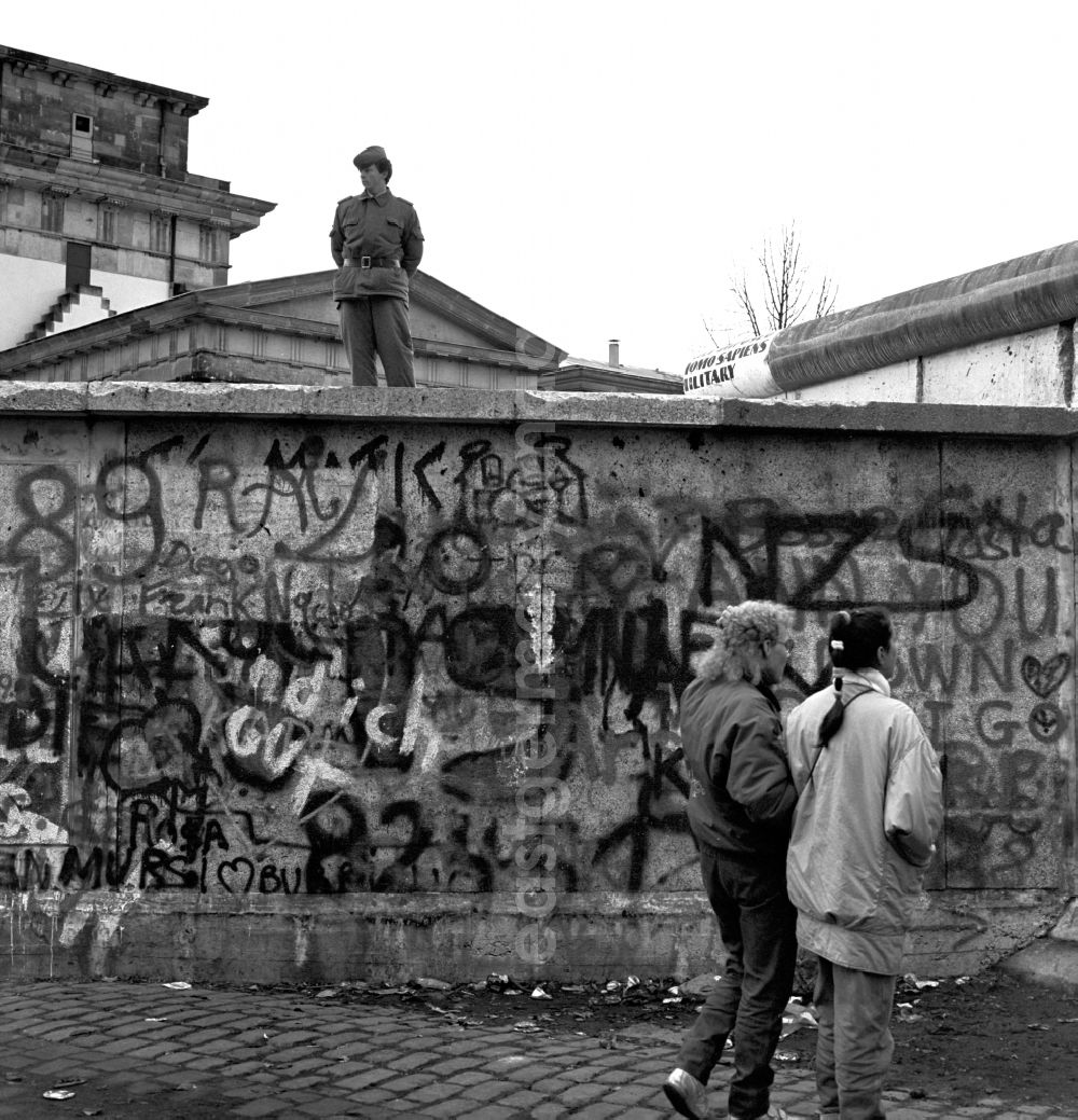 Berlin - Mitte: A soldier of the GDR border troops on the Berlin Wall at the Brandenburg Gate in Berlin. To provide some degree of order, border guards were posted on the wall. You should prevent the wall from too euphoric frontier workers is climbed