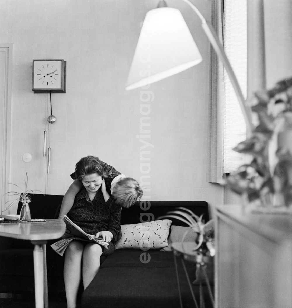 Berlin: A woman sitting on the sofa in the living room and reading a newspaper, in Berlin, the former capital of the GDR, German Democratic Republic