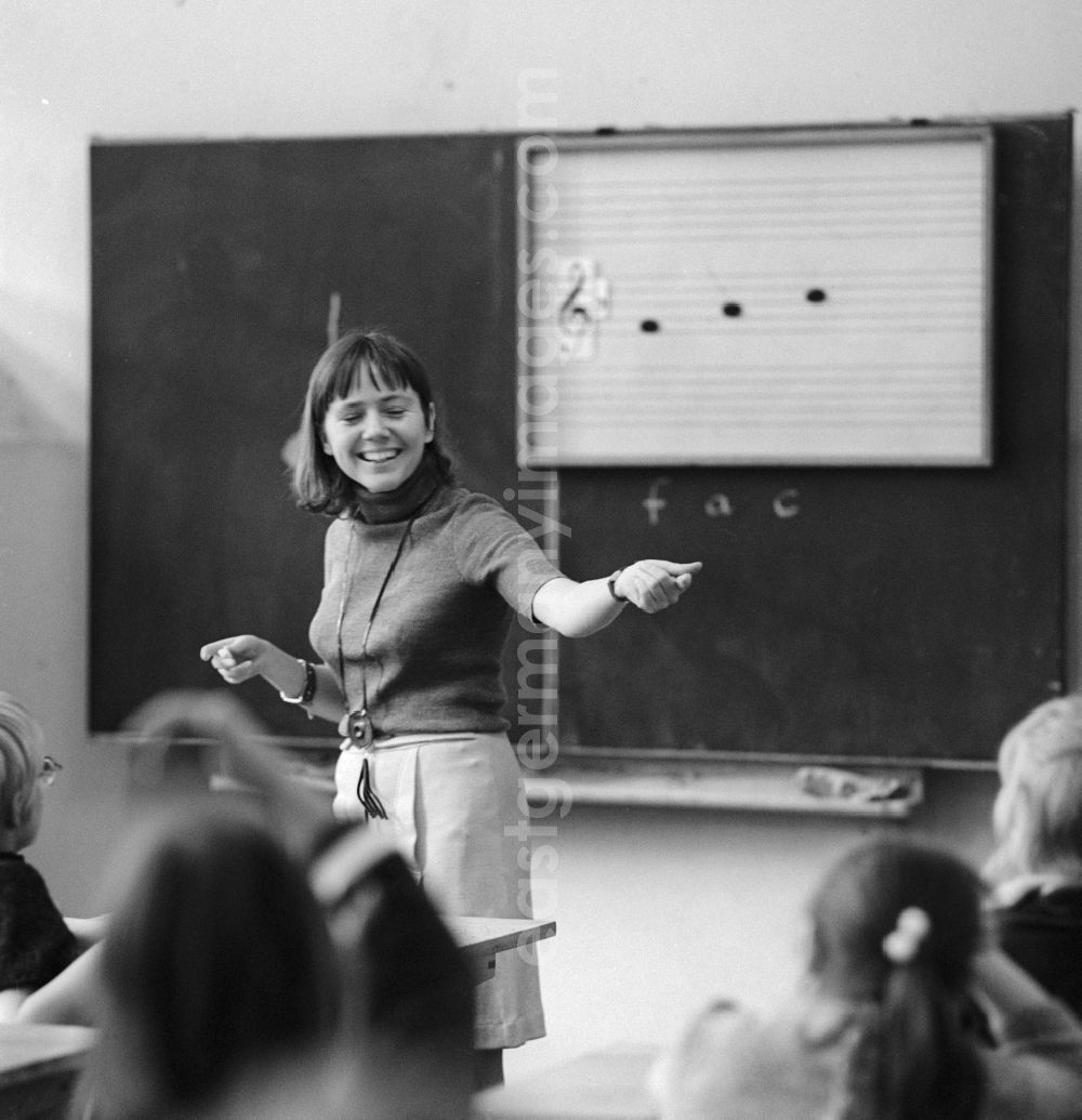 GDR photo archive: Berlin - A teacher stands in front of the class and teaches music in Berlin. On the blackboard are staves with clef and notes