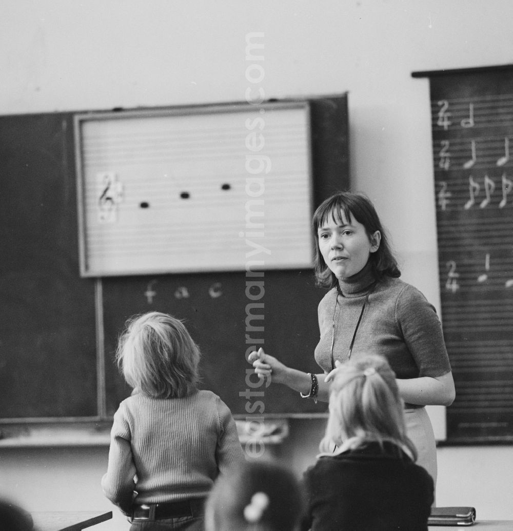 GDR picture archive: Berlin - A teacher stands in front of the class and teaches music in Berlin. On the blackboard are staves with clef and notes