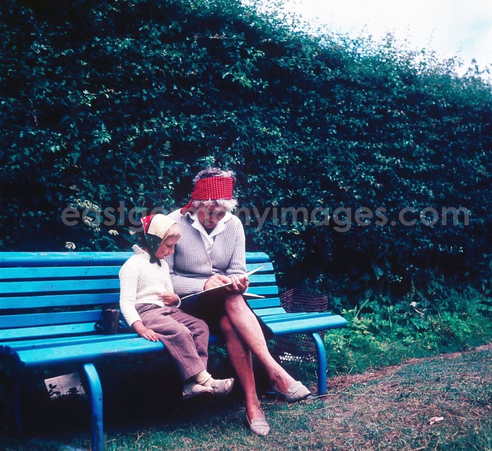 GDR photo archive: Ahrenshoop - A granny sits with her grandchild on a park-bench and they look to themselves a children's book in in Ahrenshoop in the federal state Mecklenburg-West Pomerania in the area of the former GDR, German democratic republic