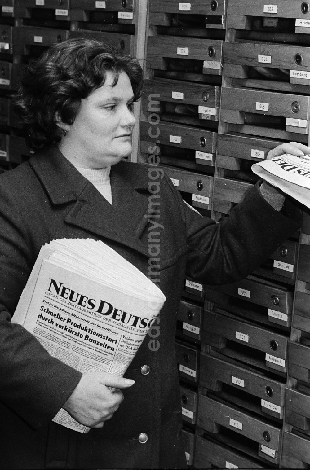 GDR picture archive: Berlin - A postal woman puts the everyday newspaper Neues Deutschland in mailbox of a block of flats in Berlin, the former capital of the GDR, German democratic republic